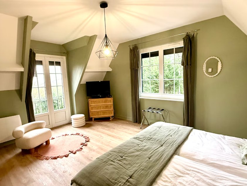 Chambre aux murs vert sauge, avec porte-fenêtre, fauteuil clair et grand lit