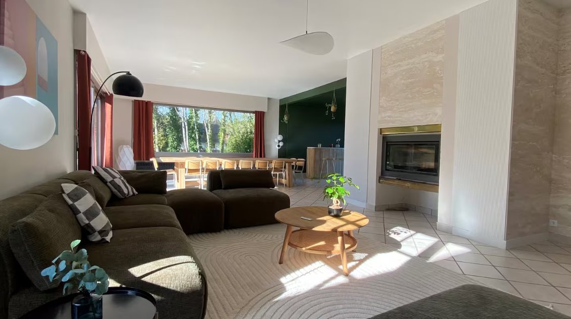 Le salon aux canapés vert kaki, avec cheminée et grande table donnant sur le jardin